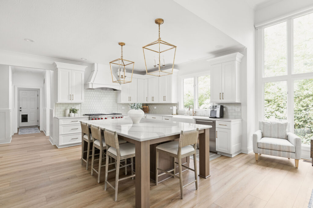 white oak kitchen island with white perimeter cabinetry and two brass island pendant lights and four bar stools
