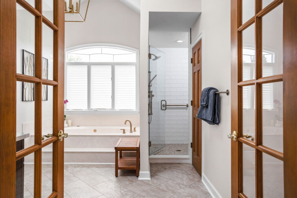 A Carmel, IN Bathroom Renovation picture showing a walk in shower an built in soaking tub. Large window over tub lets natural light flow into the neutral space.