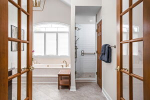 A Carmel, IN Bathroom Renovation picture showing a walk in shower an built in soaking tub. Large window over tub lets natural light flow into the neutral space.