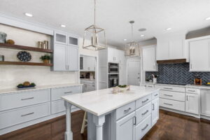 Carmel kitchen renovation refresh featuring refinished cabinetry, new buffet, bold tile, and timeless upgrades by Worthington Design & Remodeling. Photo shows buffet area to the left, island in center and range to the right. Light colored cabinetry with dark backsplash.