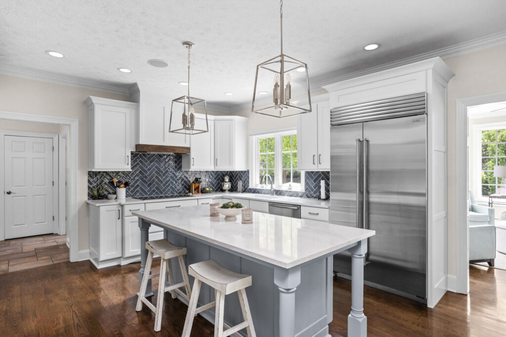 Carmel kitchen renovation refresh featuring refinished cabinetry, new buffet, bold tile, and timeless upgrades by Worthington Design & Remodeling. Photo shows light kitchen cabinetry, island with white countertops and lantern style pendant lighting. Dark backspash.