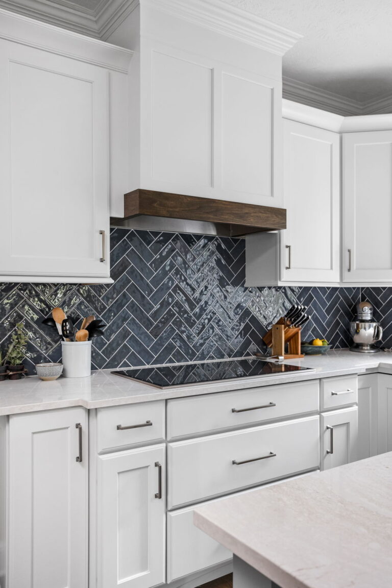 Carmel kitchen renovation refresh featuring refinished cabinetry, new buffet, bold tile, and timeless upgrades by Worthington Design & Remodeling. Photo shows close up of range area. Light cabinetry, wood hood with wood stained mantel and dark backsplash.