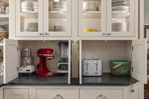 Appliance garage open, showing everyday small appliances neatly stored beneath glass-front upper cabinets.