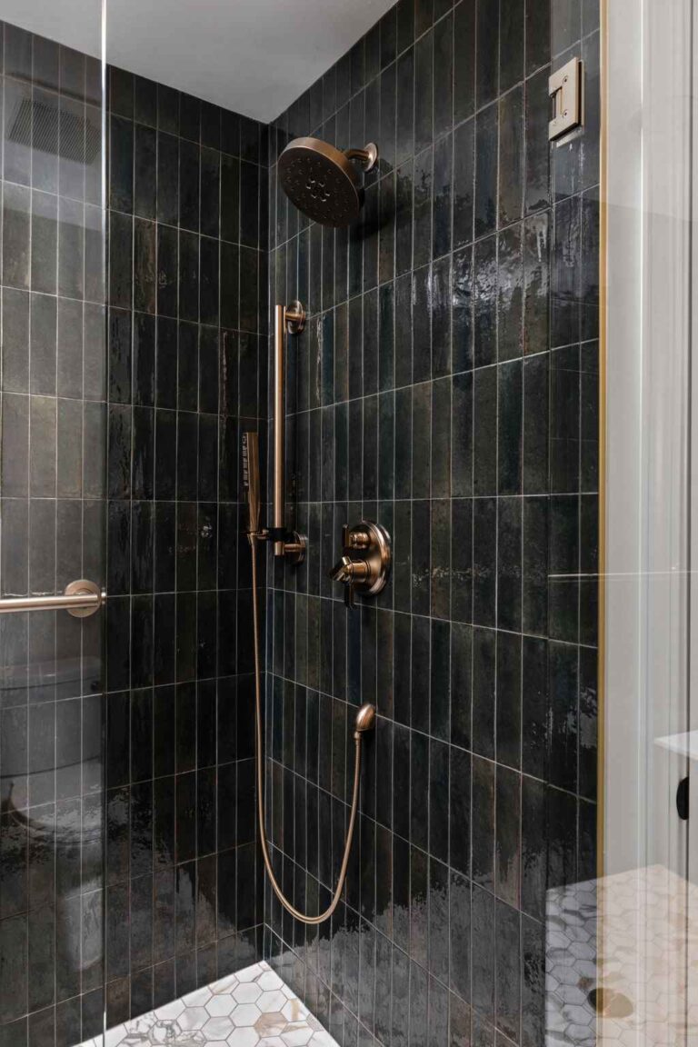 Close up of dark vertical shower tile with brass rain showerhead and handheld sprayer in a remodeled bathroom in Zionsville IN.