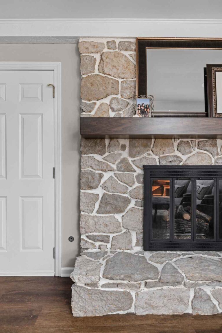 Close up of stone fireplace with dark wood mantel and family photos in a updated hearth room in Zionsville IN main level remodel.