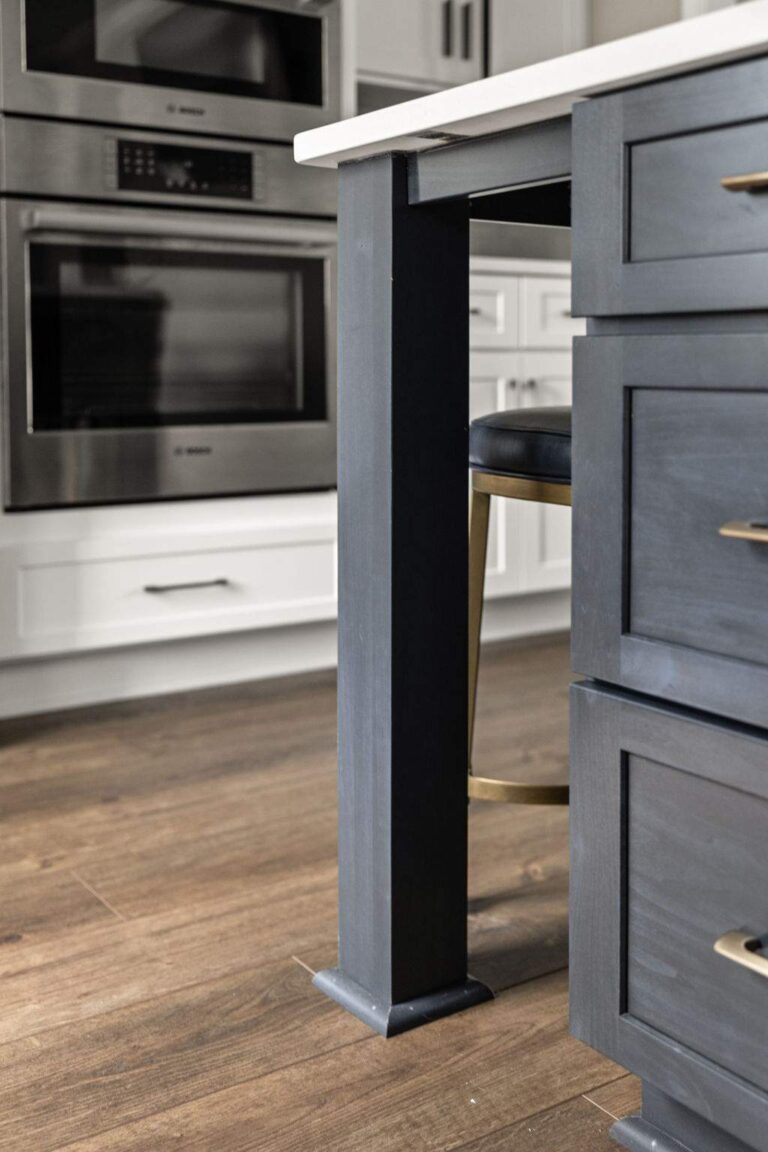 Detail of navy kitchen island leg, blue bar stool, and wood floors highlighting custom cabinetry in a main level remodel in Zionsville IN.