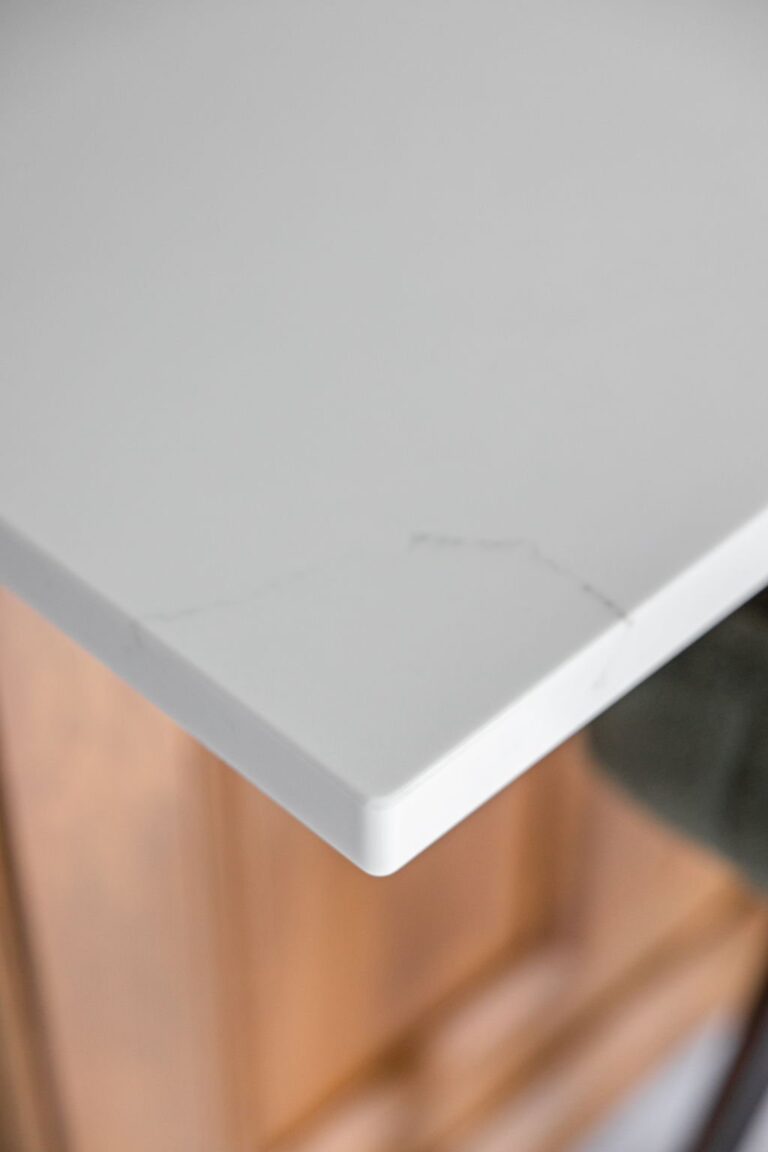 Close up of white quartz countertop corner with softly rounded edge in a repurposed oak cabinet kitchen.