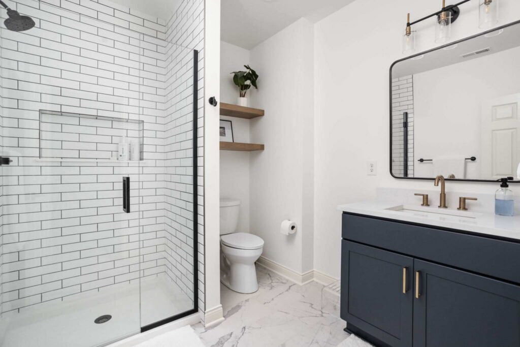 Basement bathroom renovation in Carmel Indiana featuring navy vanity cabinetry, champagne bronze fixtures, and tiled walk-in shower.