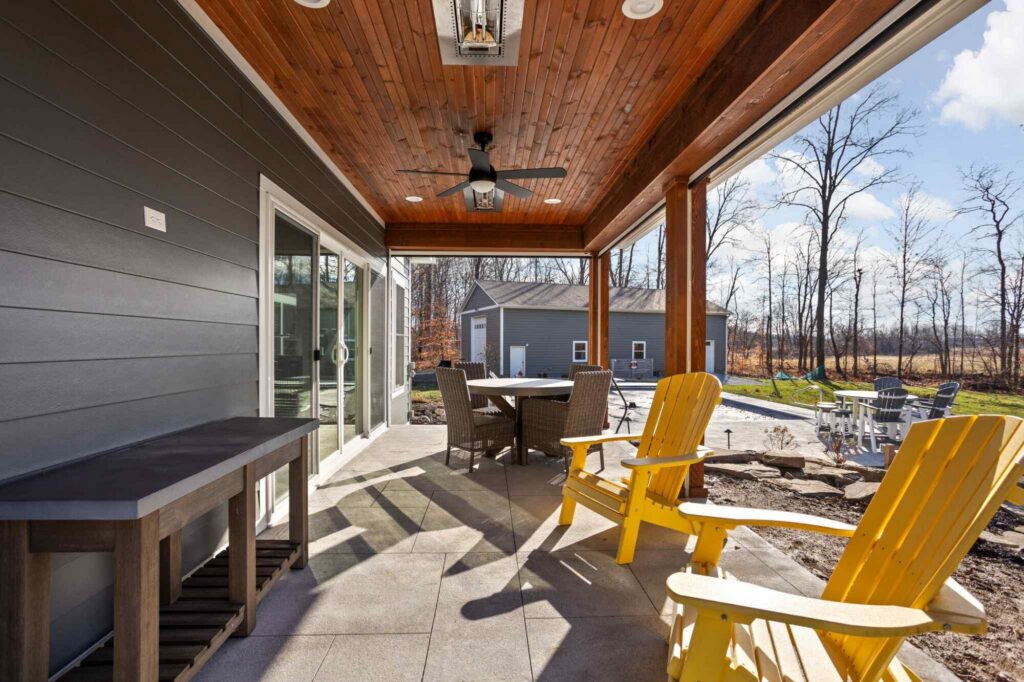 Covered patio seating area under wood ceiling with fan, looking out to the backyard, four season room addition