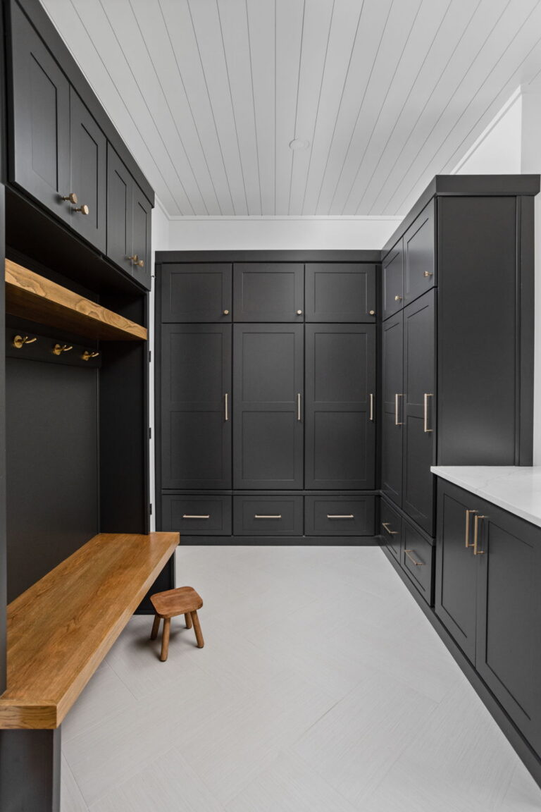 an organized laundry room remodel in carmel indiana with custom cabinetry in gray and custom cabinetry inserts of trash drawers, folding trays, pet feeding station drawer, soaking sink, drawer drying racks, white countertops and a mudroom incorporated with broom storage