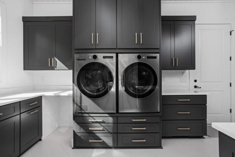 an organized laundry room remodel in carmel indiana with custom cabinetry in gray and custom cabinetry inserts of trash drawers, folding trays, pet feeding station drawer, soaking sink, drawer drying racks, white countertops and a mudroom incorporated with broom storage