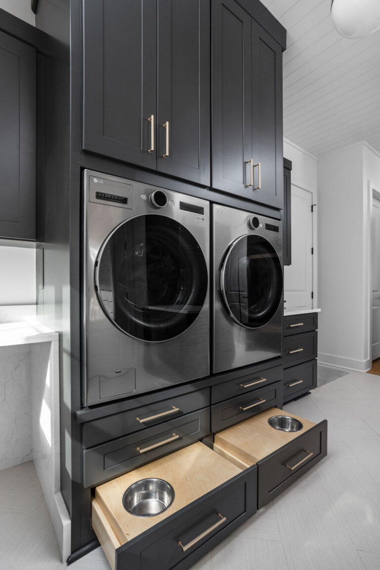 an organized laundry room remodel in carmel indiana with custom cabinetry in gray and custom cabinetry inserts of trash drawers, folding trays, pet feeding station drawer, soaking sink, drawer drying racks, white countertops and a mudroom incorporated with broom storage