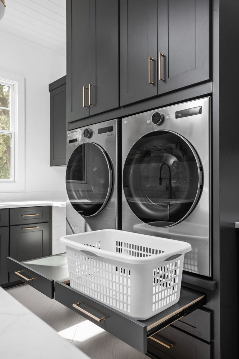 an organized laundry room remodel in carmel indiana with custom cabinetry in gray and custom cabinetry inserts of trash drawers, folding trays, pet feeding station drawer, soaking sink, drawer drying racks, white countertops and a mudroom incorporated with broom storage