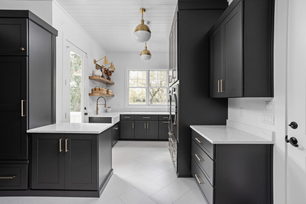 an organized laundry room remodel in carmel indiana with custom cabinetry in gray and custom cabinetry inserts of trash drawers, folding trays, pet feeding station drawer, soaking sink, drawer drying racks, white countertops and a mudroom incorporated with broom storage