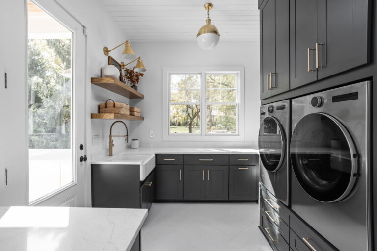 an organized laundry room remodel in carmel indiana with custom cabinetry in gray and custom cabinetry inserts of trash drawers, folding trays, pet feeding station drawer, soaking sink, drawer drying racks, white countertops and a mudroom incorporated with broom storage