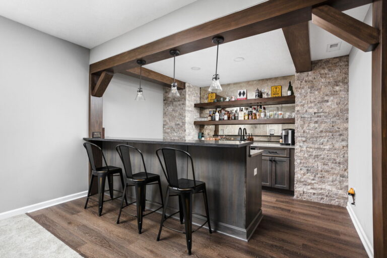 Custom basement wet bar with seating, floating shelves, stone accents, and pendant lighting in Westfield IN