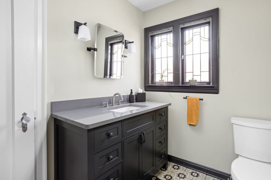 Hall bath vanity with dark painted cabinets, quartz countertop, brushed nickel faucet, and patterned tile floor by Worthington Design and Remodeling