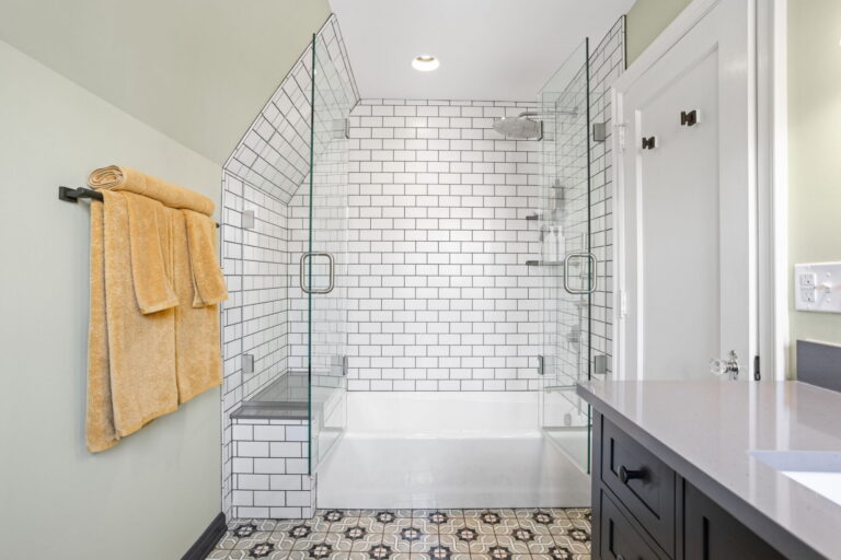 Custom hall bath remodel with glass enclosed tub shower, white subway tile walls, built in bench, and decorative floor tile