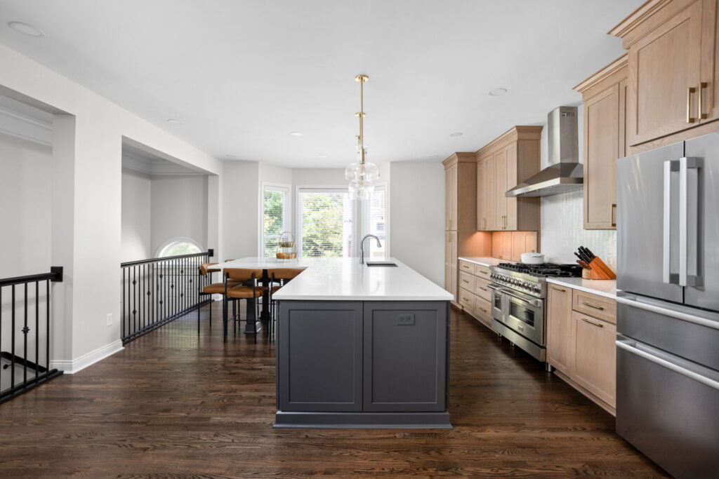 High end kitchen remodel Carmel with a long charcoal island, white quartz countertops, light wood cabinetry, and open layout overlooking the stair rail.