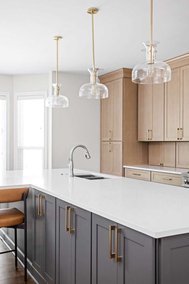 High end kitchen remodel Carmel with a large dark island, white quartz countertop, brass pendant lights, and light red oak wood perimeter cabinetry.