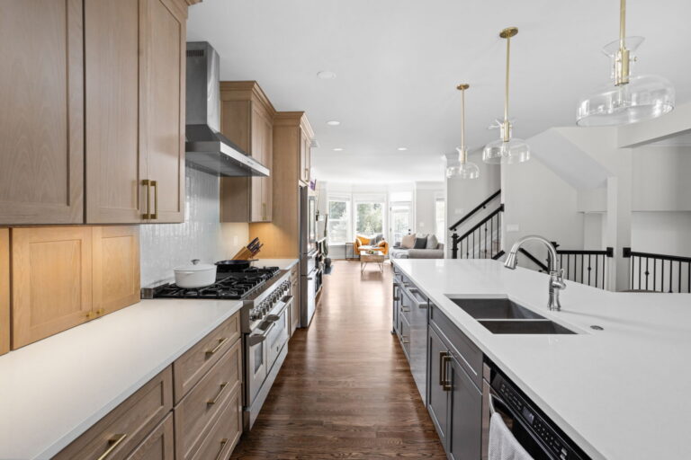 High end kitchen remodel Carmel with a galley style view of the kitchen, waterfall style island sink area, light wood perimeter cabinetry, and open sightline to the living room.