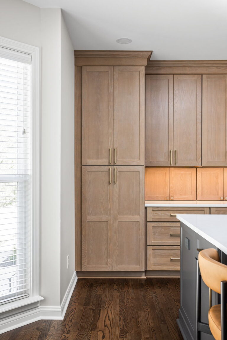 High end kitchen remodel Carmel showing tall light red oak wood pantry cabinetry, integrated storage, and a dark painted island with white countertop.