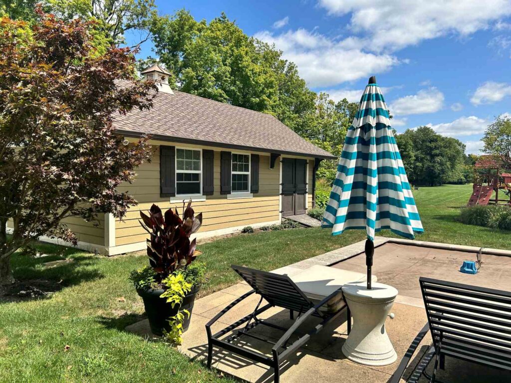 picutre of a pool house renovation before any remodeling took place a separate shed from the pool area separated by grass and a covered pool with tired landscaping