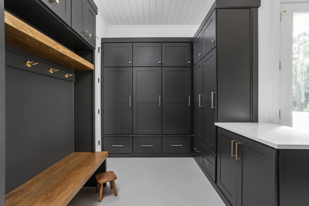 an organized laundry room remodel in carmel indiana with custom cabinetry in gray and custom cabinetry inserts of trash drawers, folding trays, pet feeding station drawer, soaking sink, drawer drying racks, white countertops and a mudroom incorporated with broom storage