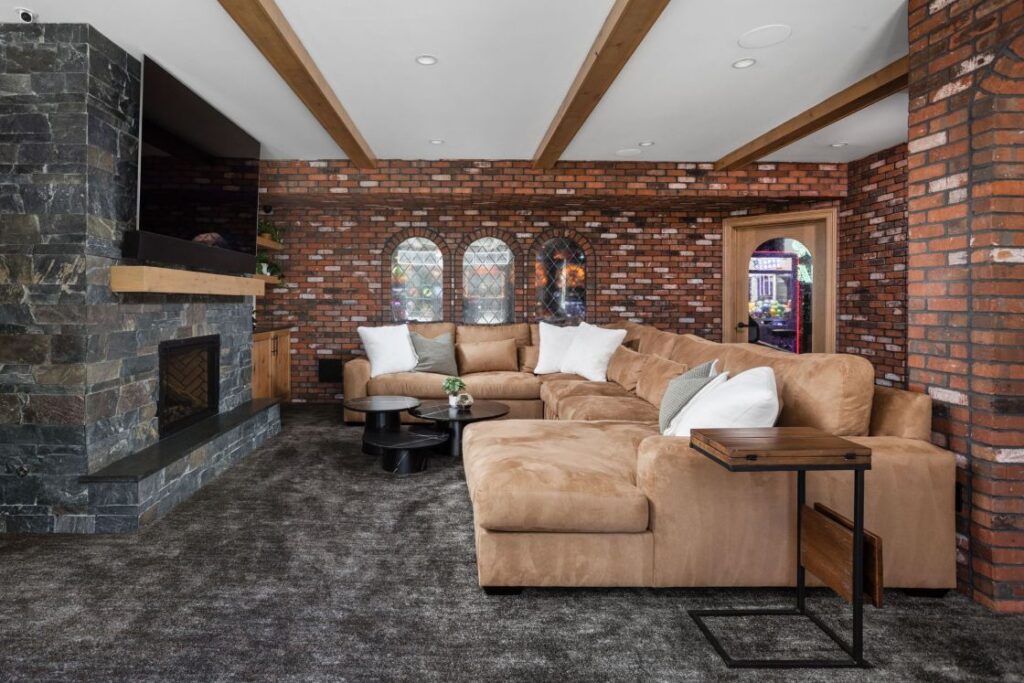 The inviting living room area features a stunning Emser Stone fireplace surround and a custom wood mantel during this luxury Zionsville basement remodeling project.