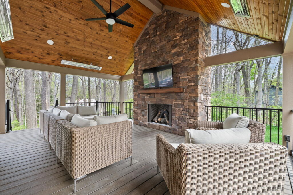 Carmel covered deck remodel with stone fireplace, outdoor seating, cedar ceiling, black railing, and Trex composite decking.