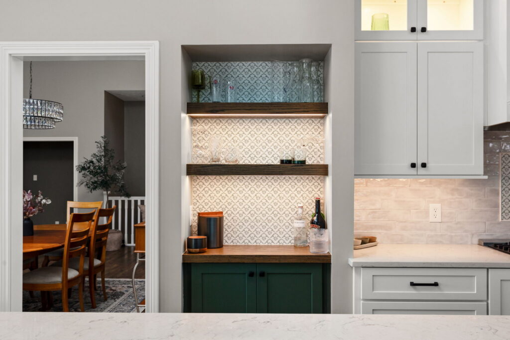 Lighted kitchen nook in Fishers with stained floating shelves, patterned tile backsplash, and green base cabinetry.