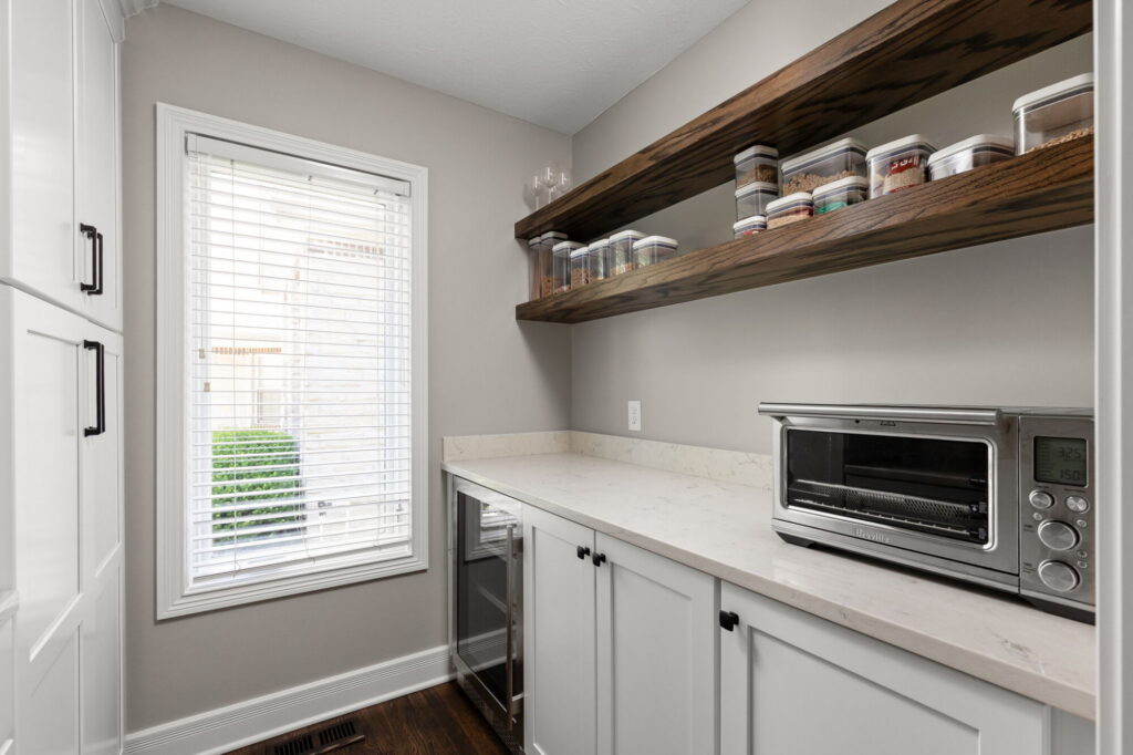 Finished Fishers pantry remodel with MSI Carrara Miksa quartz, white cabinetry, wood floating shelves, and beverage storage.