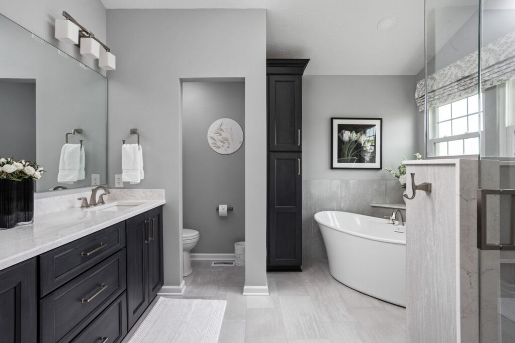 Finished Fishers primary bathroom remodel with dark Shiloh vanity cabinetry, Cambria Dovestone quartz, large mirror, and updated toilet room.
