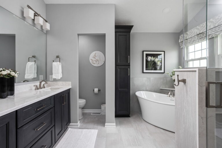 Finished Fishers primary bathroom remodel with dark Shiloh vanity cabinetry, Cambria Dovestone quartz, large mirror, and updated toilet room.
