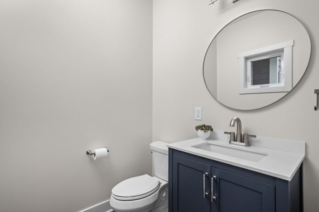 New powder bathroom in Indianapolis remodel with OVE Decors midnight blue vanity, Delta faucet, and round mirror.
