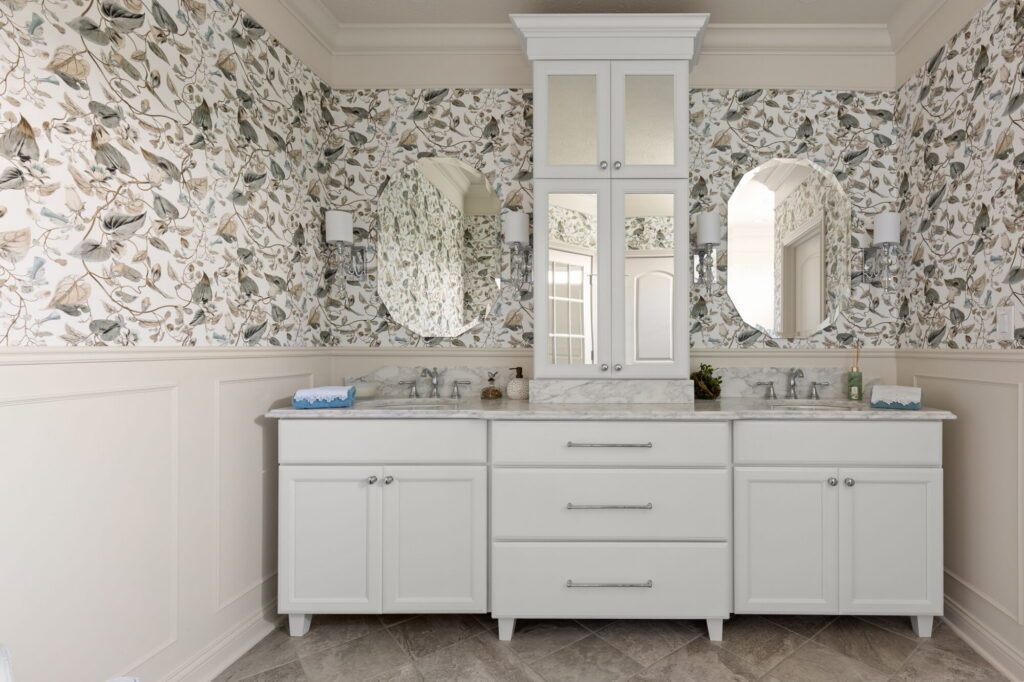 Luxury primary bathroom remodel in Westfield IN with Shiloh Pure White cabinetry, MSI Calacatta Ocellio quartz, floral wallpaper, and polished chrome sconces.
