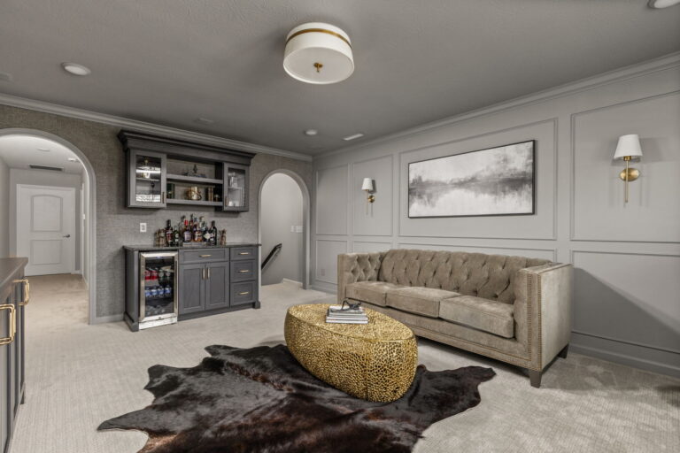 Finished Fishers, Indiana custom home bar remodel with lounge seating, dry bar cabinetry, picture molding, brass sconces, arched opening, and tailored millwork.