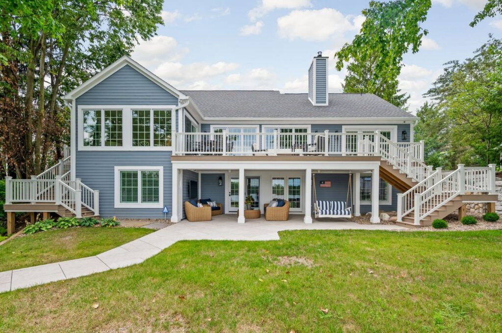 Rear exterior of the Nantucket Bay whole-house remodel with upper Trex deck, covered lower patio and lakefront outdoor living areas.