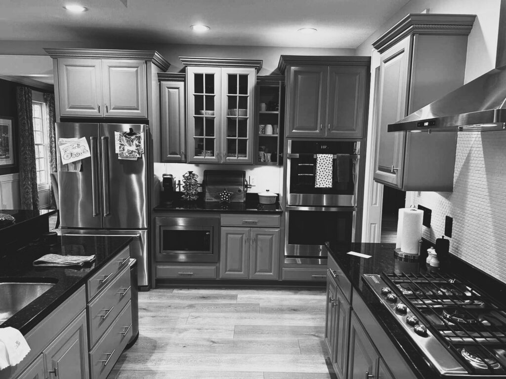 Before: Carmel kitchen appliance wall with gray cabinetry, dark countertops, refrigerator and stacked ovens.
