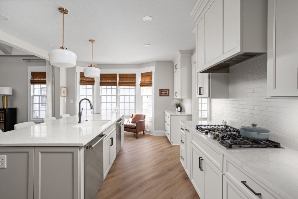 After: White Carmel kitchen with a large island opposite the gas cooktop wall and bay windows beyond.
