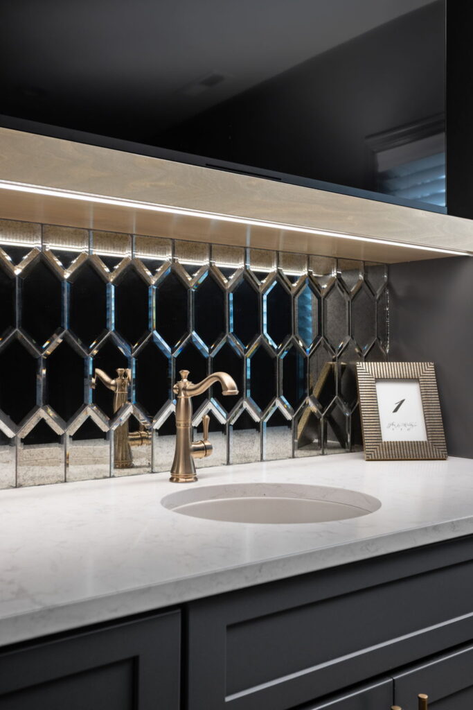 Round undermount bar sink with a bronze faucet, beveled mirrored backsplash and lighting beneath the wood shelf.