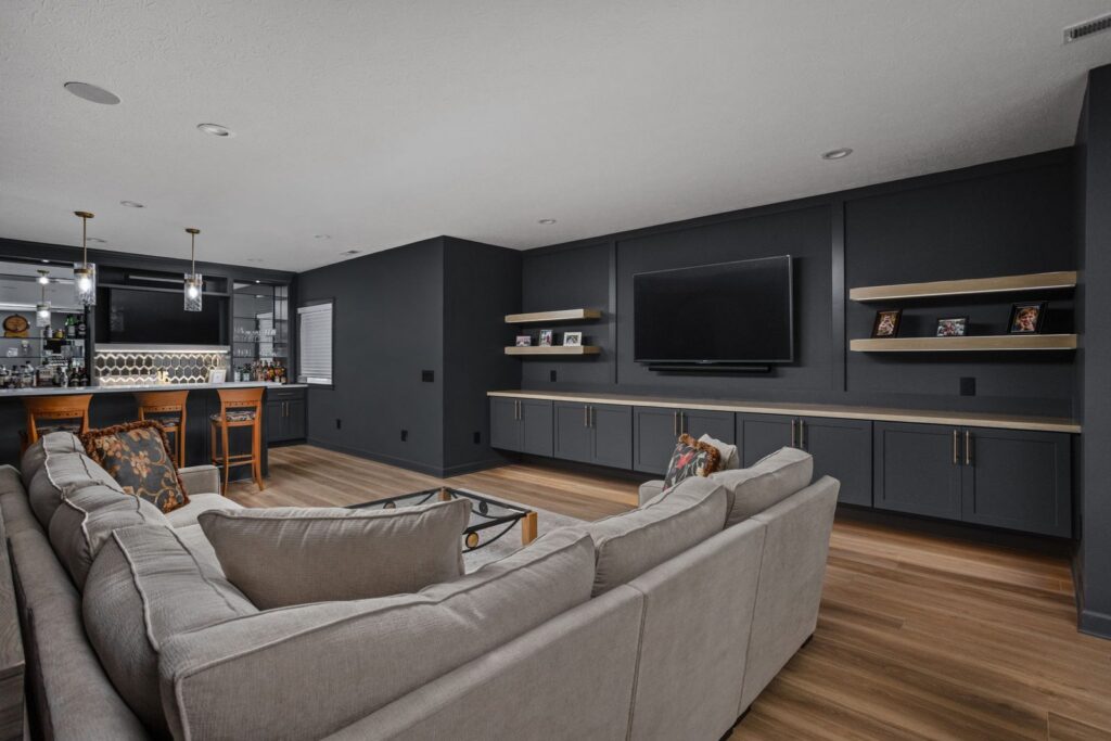 After: Basement seating area facing a wet bar and TV wall with matching dark cabinets and wood shelves.