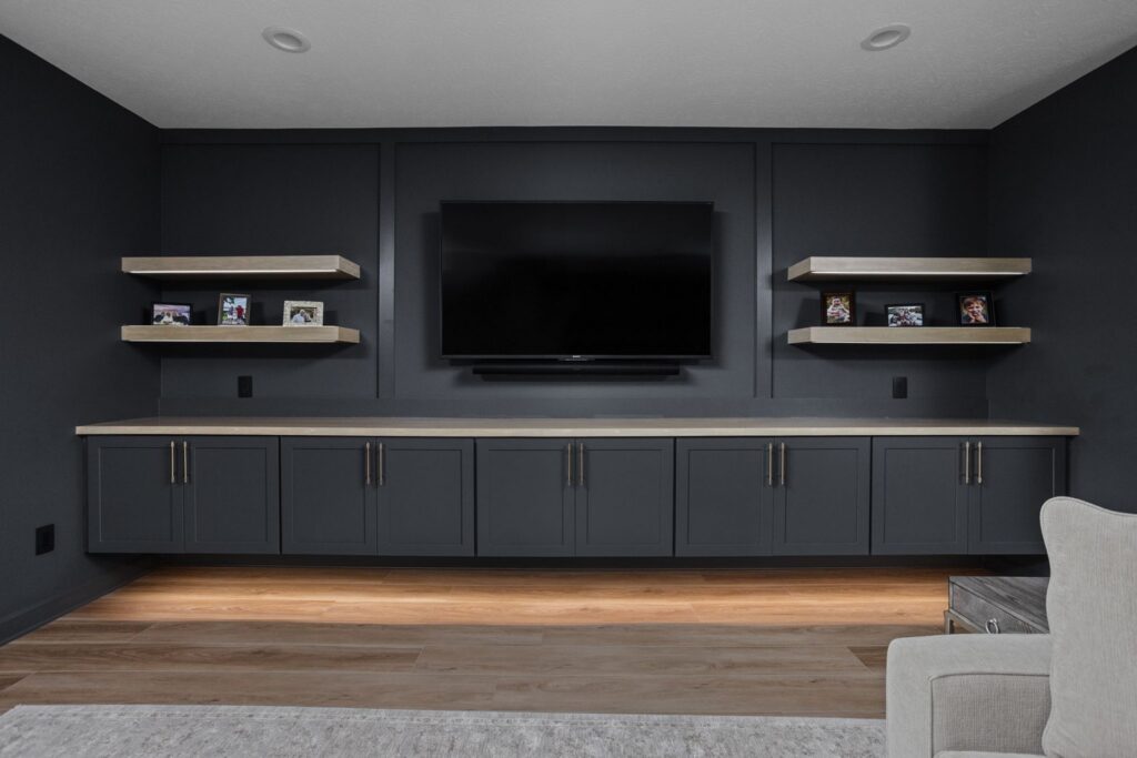 Wall-mounted TV above floating dark cabinets, with a wood countertop, four wood shelves and undercabinet lighting.