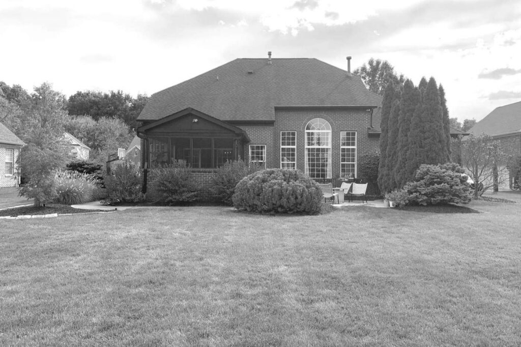 Before: Carmel backyard with a small patio beside the screened porch and shrubs along the house.