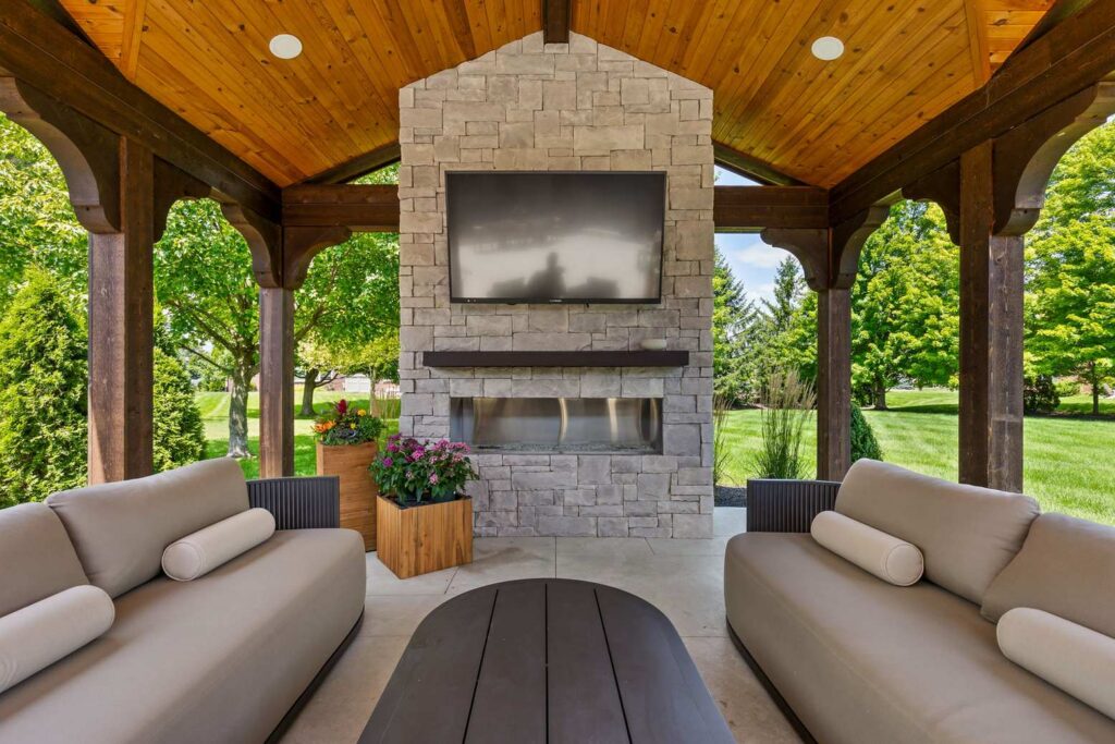 Stone fireplace and television centered between two sofas beneath a vaulted wood pavilion ceiling.