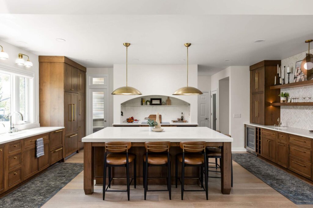 Carmel kitchen with an arched white hood, wood cabinetry, a quartz island and brass pendant lights.