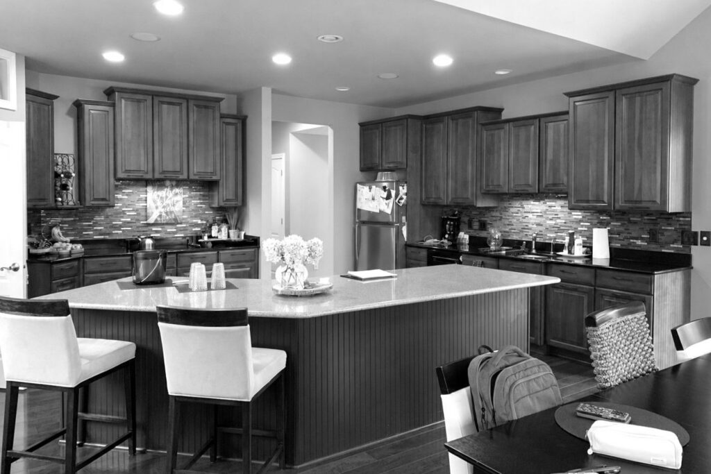 Carmel kitchen with a central island, wood cabinets, a cooktop beneath upper cabinets and a doorway beside the cooking wall.
