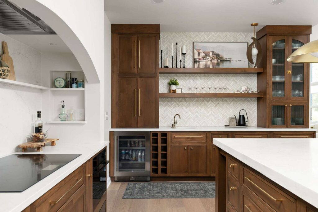 Kitchen beverage station with wood cabinets, open shelves, a small sink, beverage refrigerator and herringbone tile.