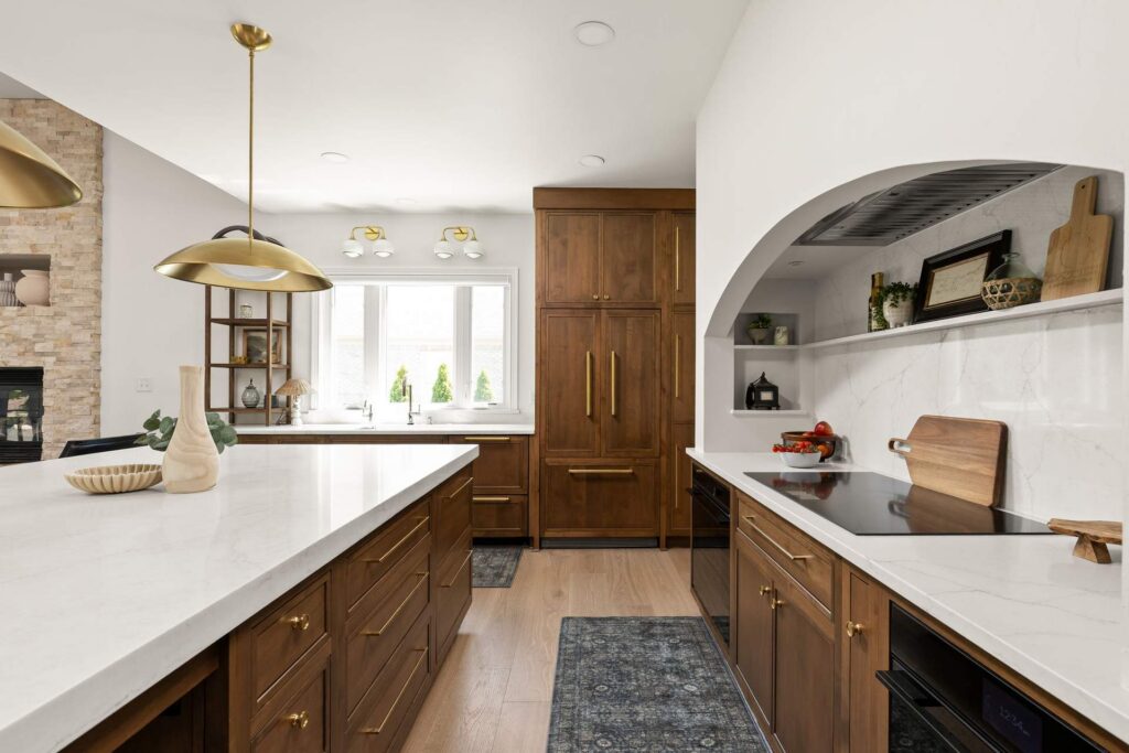 Induction cooktop beneath an arched hood, opposite a wood kitchen island, with the sink window and paneled refrigerator beyond.