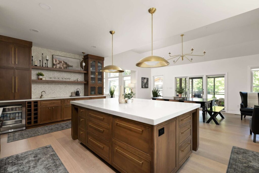 Wood kitchen island with drawer storage, a pale quartz countertop and brass pendant lights beside the dining area.